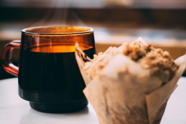 A steaming mug and a muffin on a table.