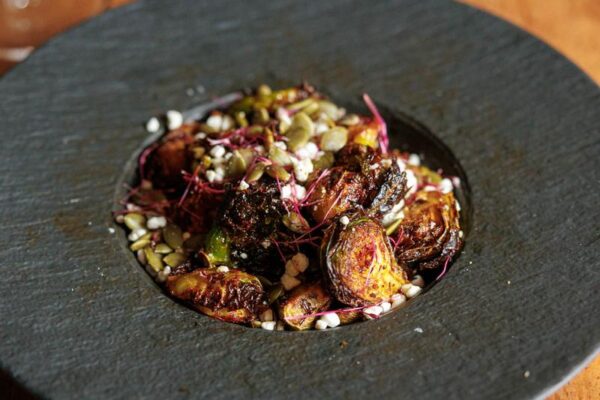 A dark, back bowl of dressed up Brussels sprouts.