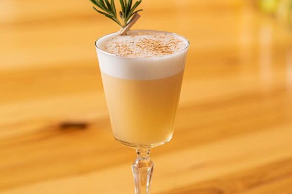 A yellow-orange drink with a green garnish served at Cafe Vino in a long stem glass.